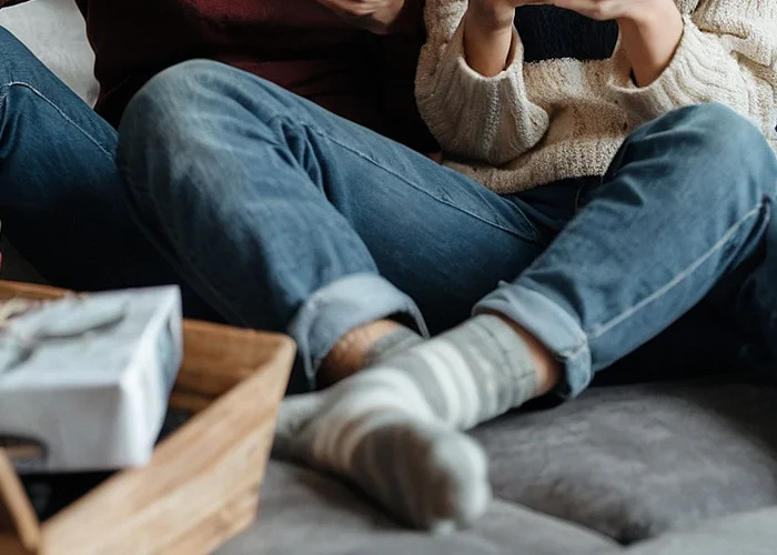 Junge Frau in blauer Jeans und mit Socken sitzt auf der Couch und ist an ihrem Smartphone